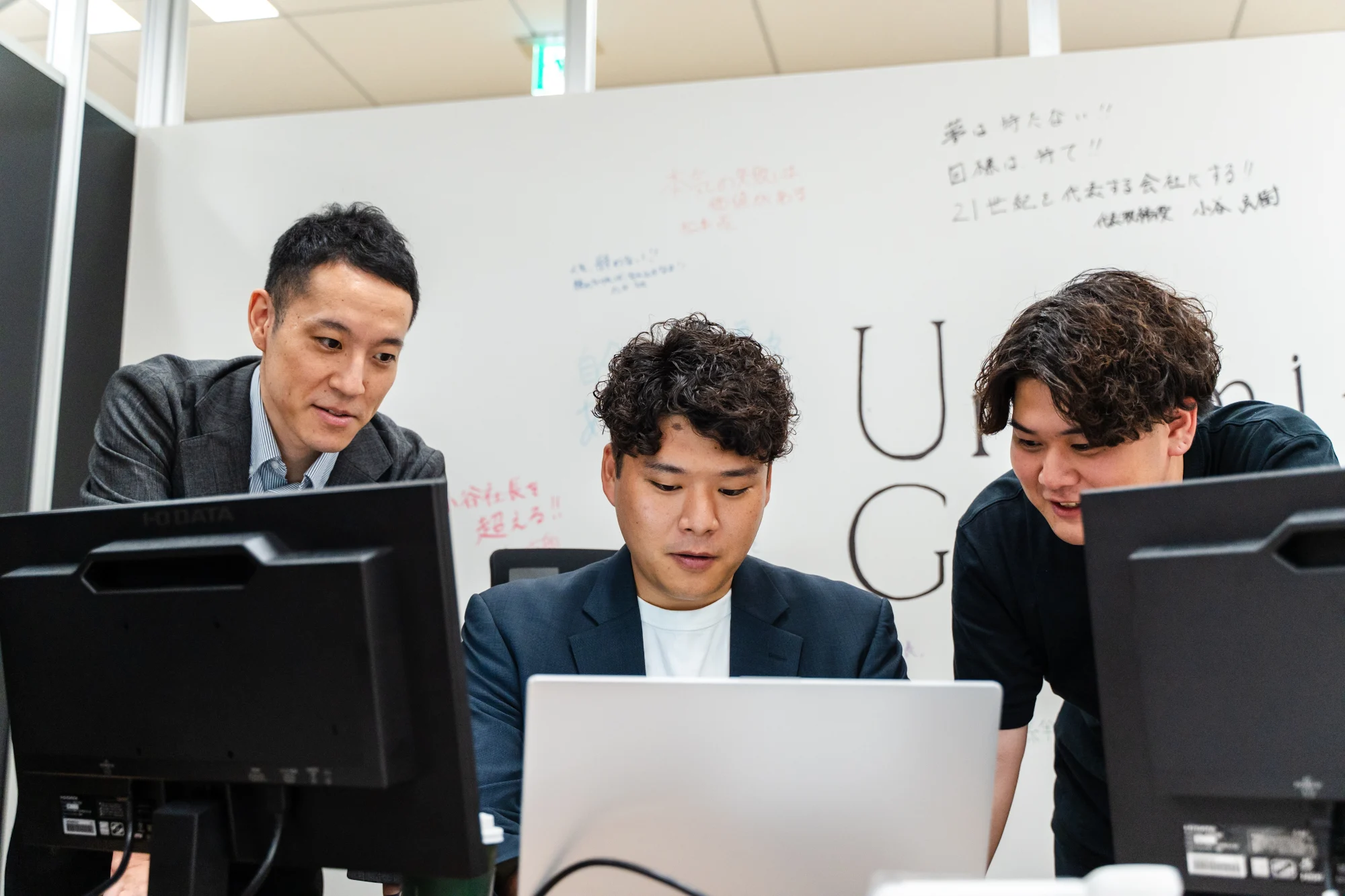 ホワイトボードの前で画面を見ながら議論するUnlimited Glowthのメンバー
